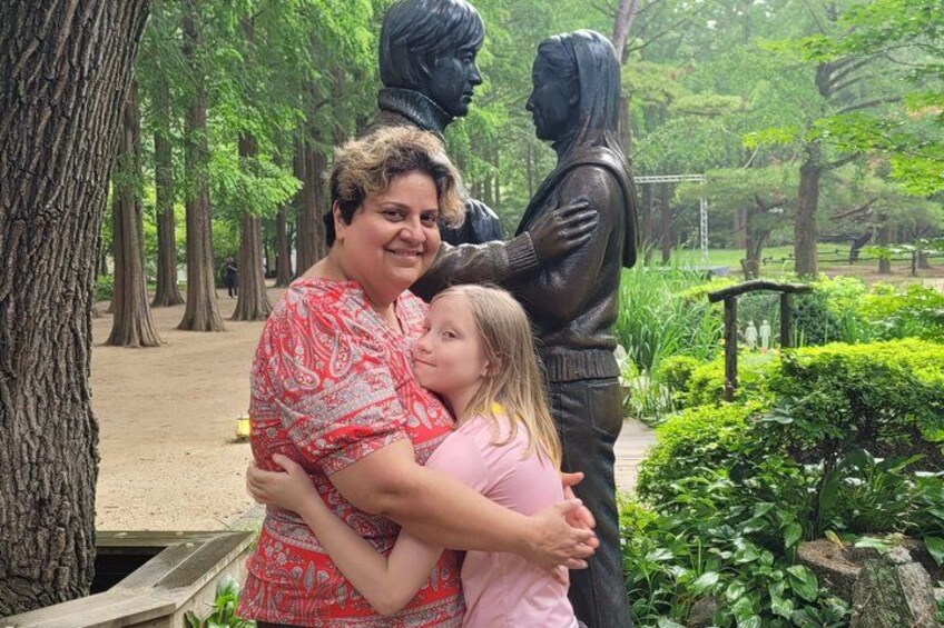 A person hugging a statue in a park with trees and greenery. 2