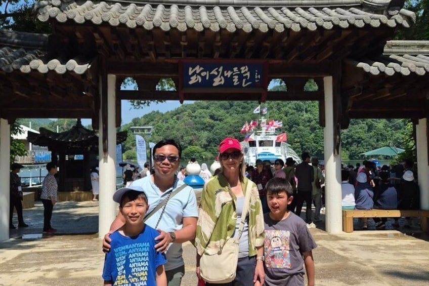 A traditional Korean pavilion with a sign, people, and a boat in the background. 2