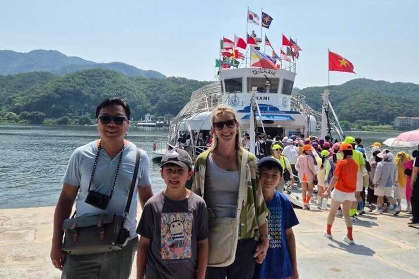 A group of people on a boat with flags, a lake, and mountains in the background. 5