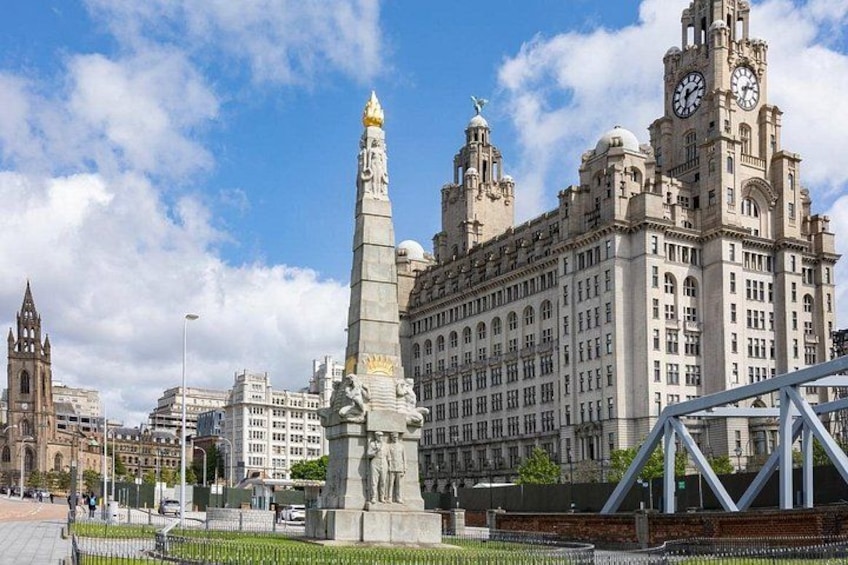 A large building with a clock tower, a monument, and a bridge. 1