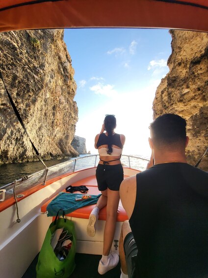 A boat with two people, one standing and one sitting, looking at a rocky coastline. 2
