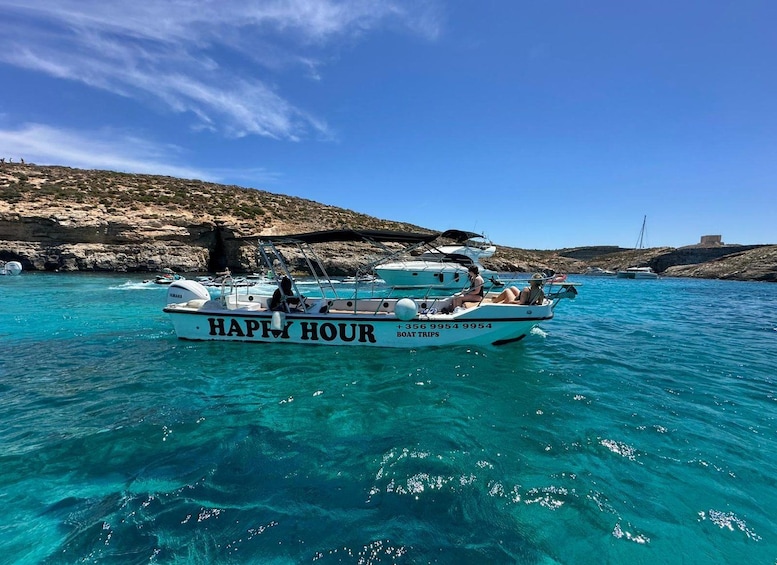 En båd ved navn 'HAPPY HOUR' på klart turkis vand med klippestykke i baggrunden. 2