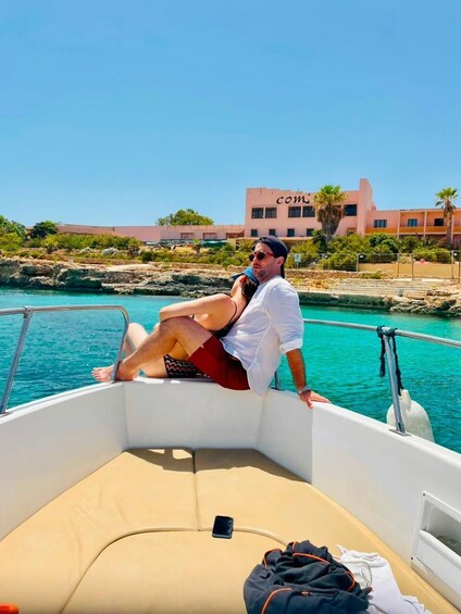 Un bateau avec une personne assise au bord, une autre personne appuyée à la rambarde, et un bâtiment en arrière-plan. 2