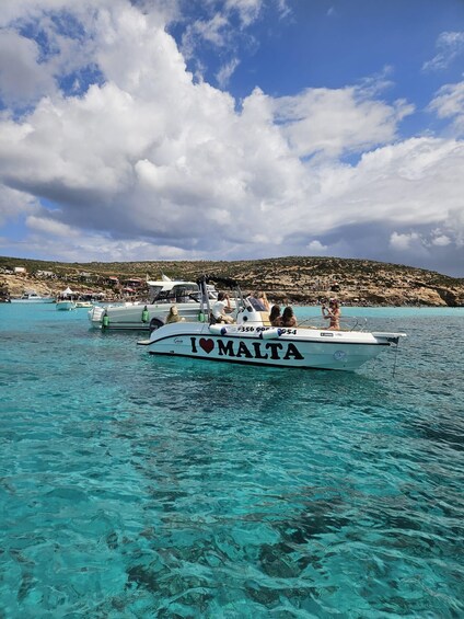 A boat with 'I ♥ MALTA' written on it, surrounded by clear turquoise water and a rocky coastline. 3