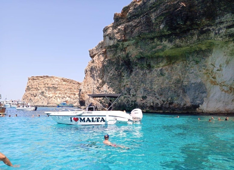 En båd med teksten 'I ♥ MALTA', en svømmer i vandet og klippefremspring i baggrunden. 5