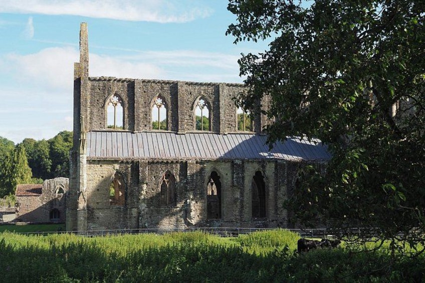 A historic stone building with arched windows and a metal roof, surrounded by greenery. 2