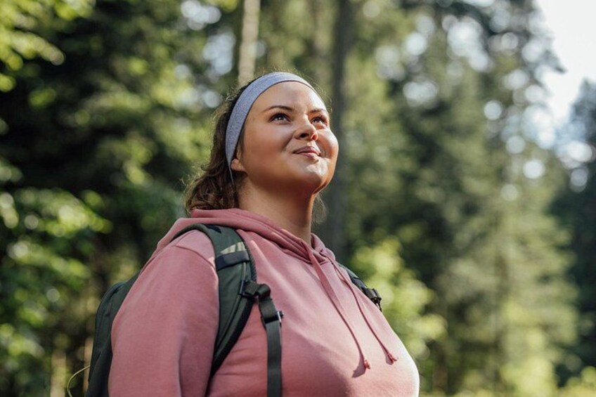 A person wearing a pink hoodie and a headband, standing in a forested area. 2