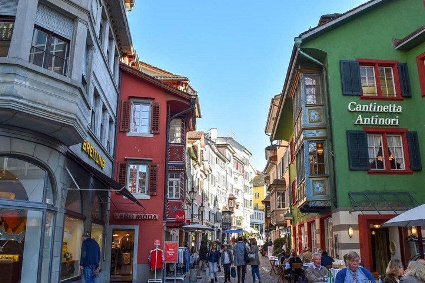 A bustling street with colorful buildings, a café named 'Cantinetta Antinori,' and a store called 'Breitling.' 4