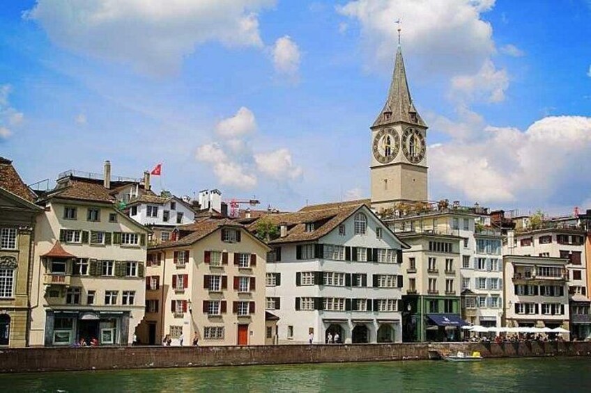 A historic town with a prominent clock tower, traditional buildings, and a river. 5