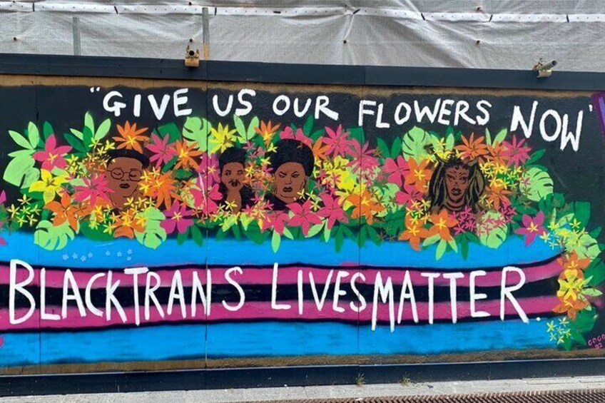 En mural med farverige blomster og tekst med påskriften "Give us our flowers now" og "Black Trans Lives Matter". 1