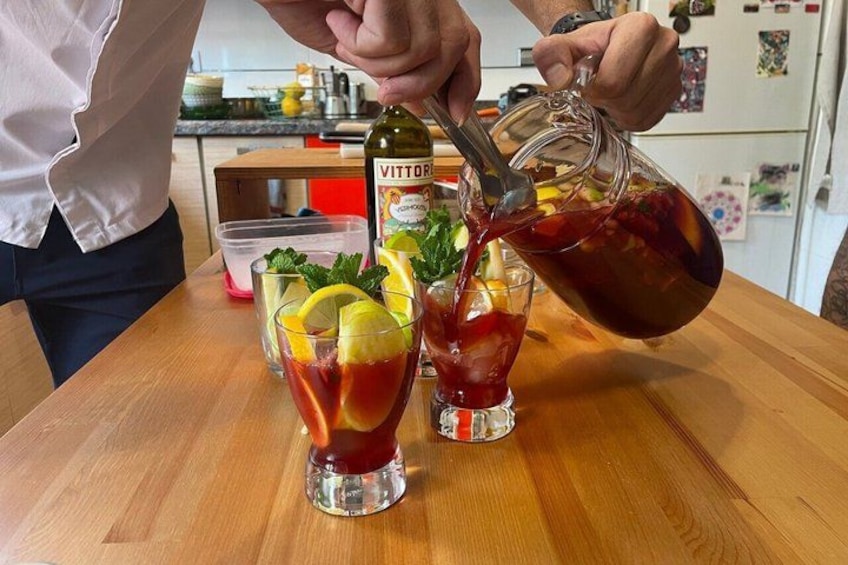 A person pouring a red liquid from a bottle into two glasses on a wooden table. 4