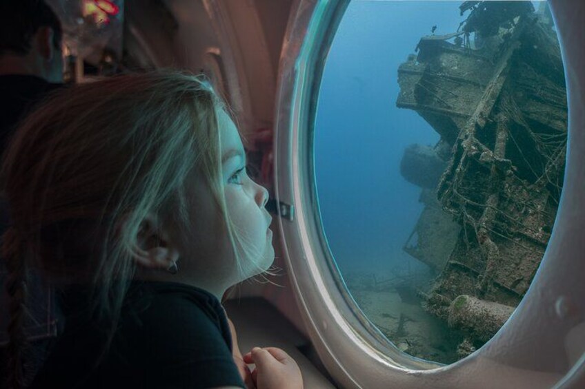 A child looking out of an airplane window at a submerged shipwreck. 4