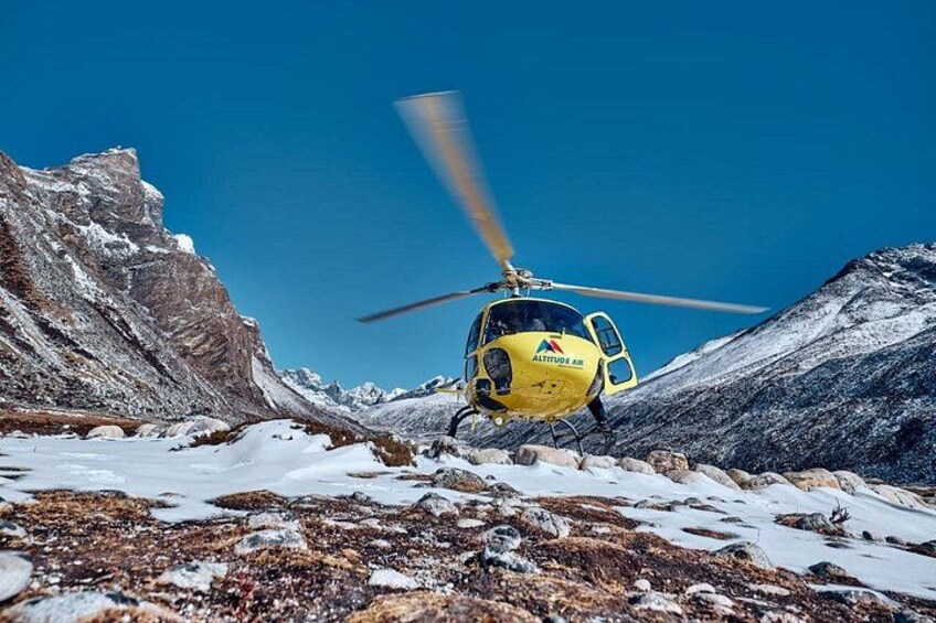 A yellow helicopter with 'ASTARUS AIR' on its side, hovering over a snowy mountainous terrain. 3