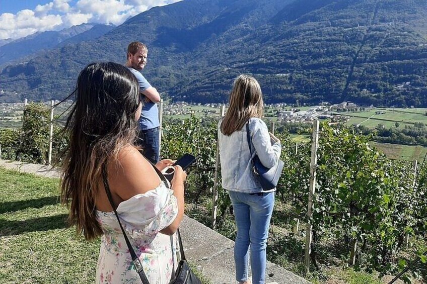 A woman taking a photo, a man standing behind her, and a scenic view of a valley with mountains in the background. 3