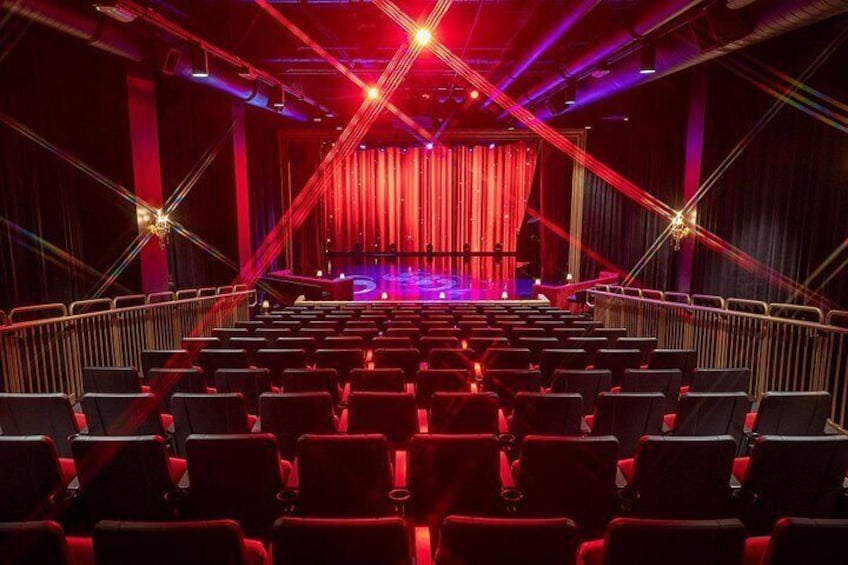 An auditorium with rows of seats, a stage with a red curtain, and stage lights. 4