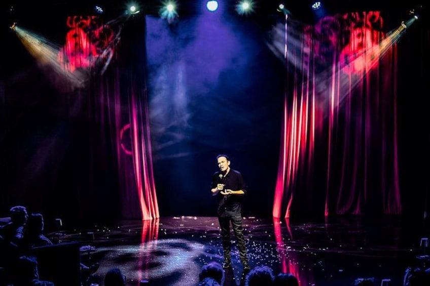 A person on stage with a microphone, surrounded by stage lights and curtains. 4