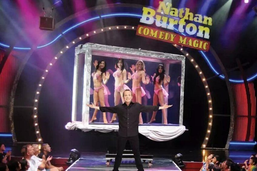 A stage with a man performing, a sign reading 'Nathan Burton Comedy Magic', and a framed picture of performers in the background. 2