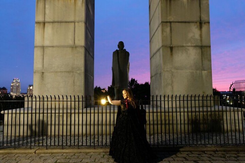 A person in a black dress standing in front of a monument with two large pillars and a statue in the center, during twilight. 3