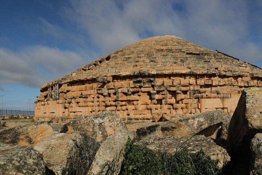 A large, ancient stone structure with a flat top and a stepped base, surrounded by large boulders. 3
