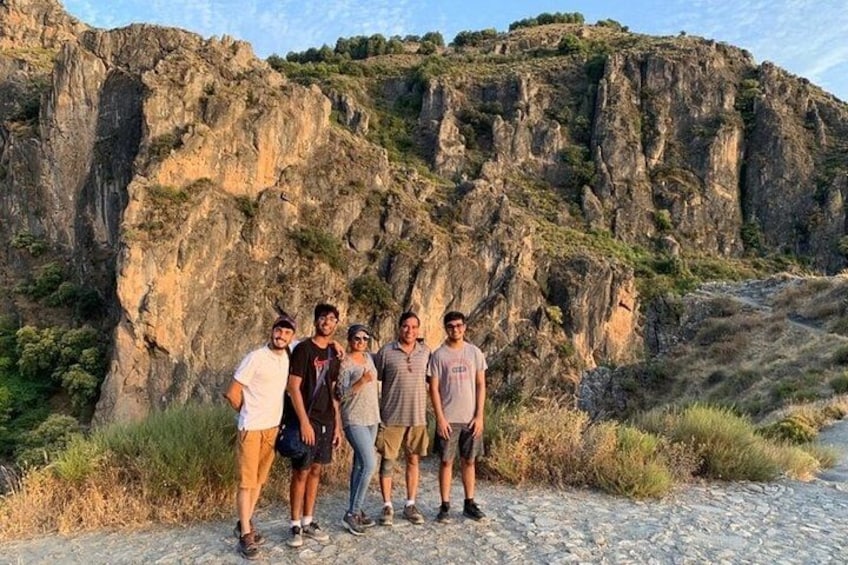 A group of people standing on a cobblestone path with a rocky cliff in the background. 2