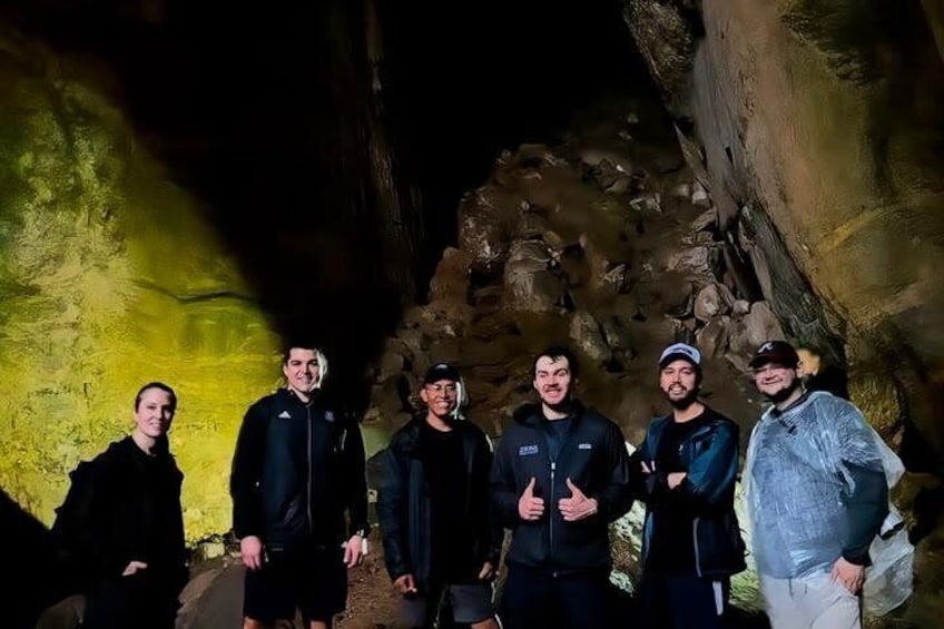 Un groupe de personnes se tient dans une grotte aux parois rocheuses, baignée d’une lumière jaunâtre. 2