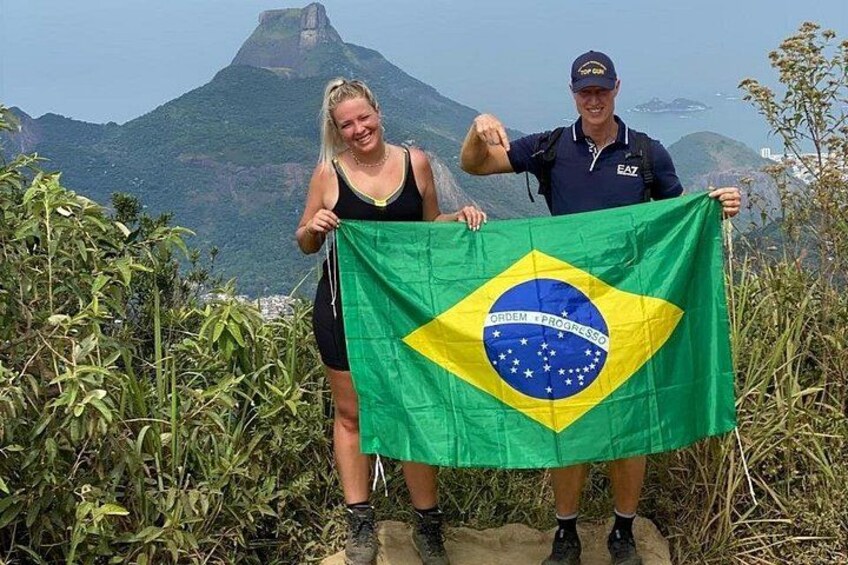 Two people holding a Brazilian flag with a mountainous landscape in the background. 4