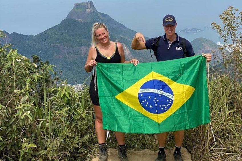 Two people holding a Brazilian flag with a mountain in the background. 3