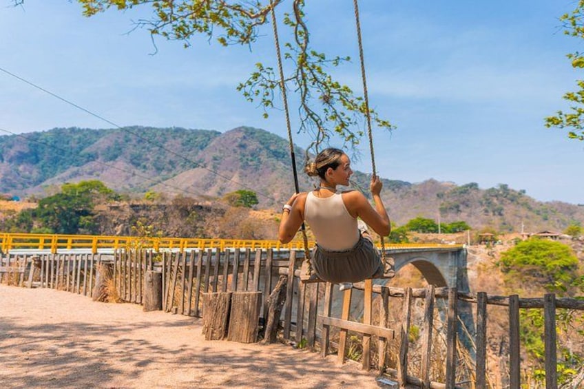 Una persona sentada en un columpio con vista a un puente y un paisaje montañoso al fondo. 3