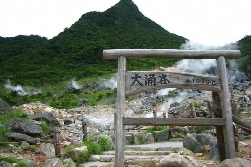 A wooden sign with Japanese characters, a mountainous landscape, and steam rising from the ground. 4