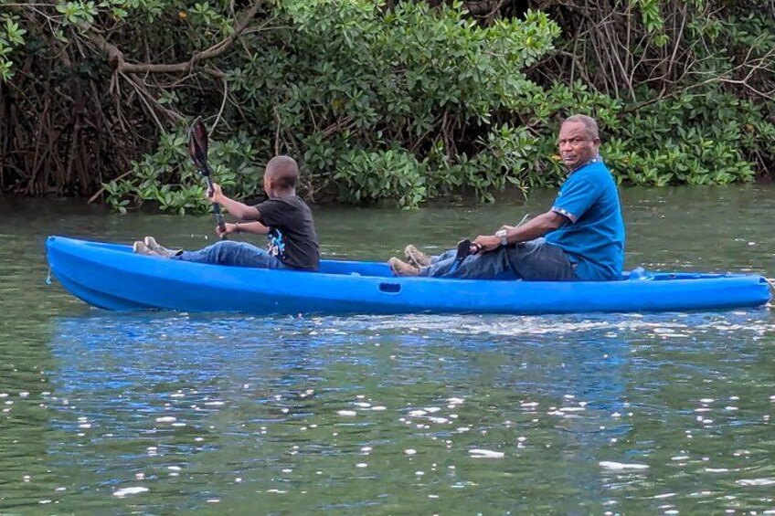 Dos personas en un canoa azul sobre un río tranquilo rodeado de densa vegetación de manglares. 3