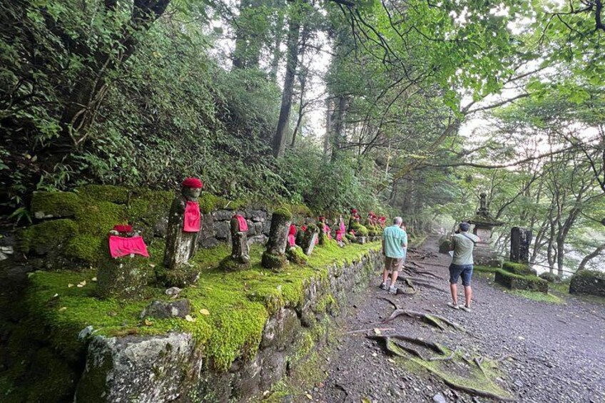 A forested path with moss-covered rocks and statues. 5