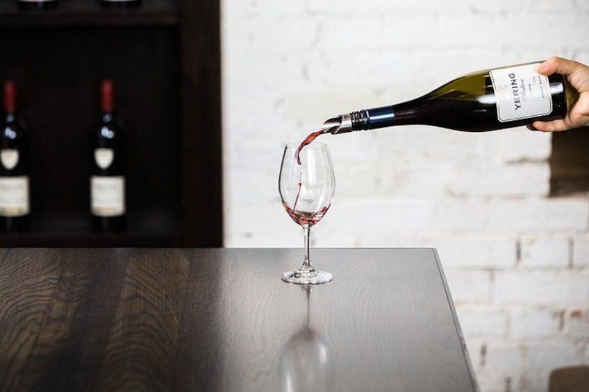A hand pouring red wine from a bottle into a glass on a wooden table. 3
