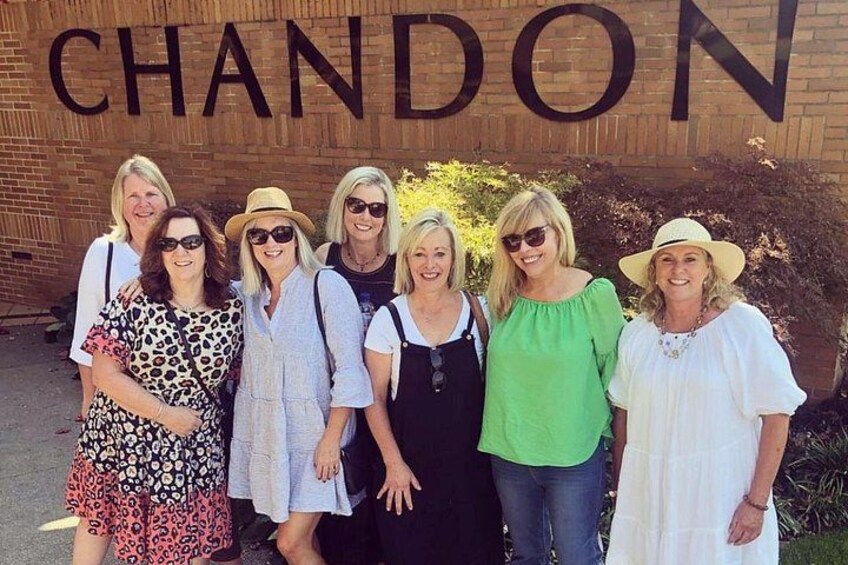 A group of people standing in front of a building with the word 'CHANDON' on the wall. 1