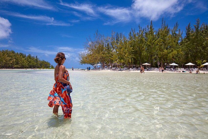 Una spiaggia con acque cristalline poco profonde, una donna con un abito colorato e ombrelloni. 2