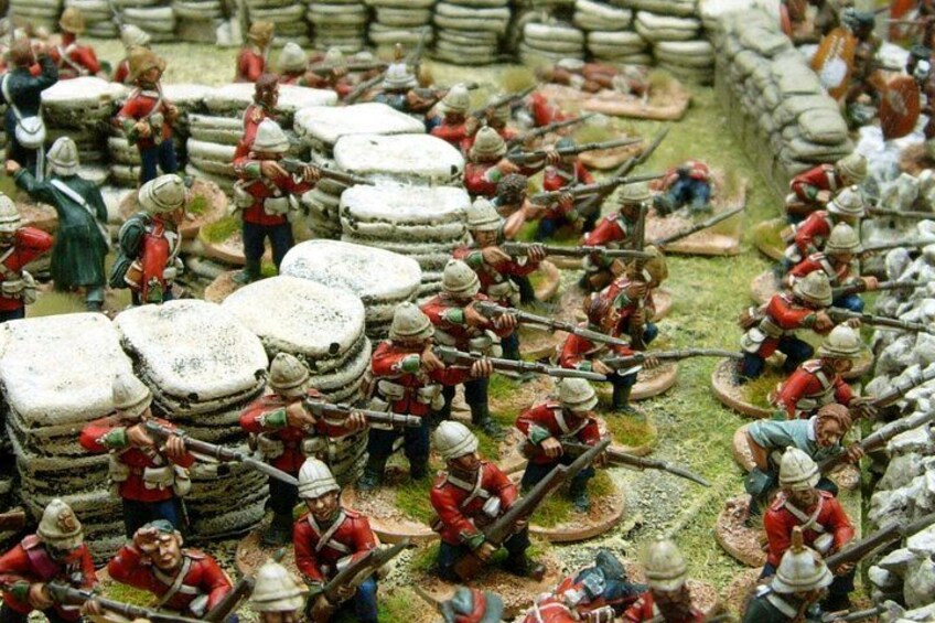 A detailed miniature battle scene with soldiers in red uniforms, some on foot and others on horseback, amidst stacks of ammunition and a trench. 1