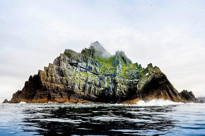 A rocky island with a waterfall in the foreground and a mountain in the background. 3