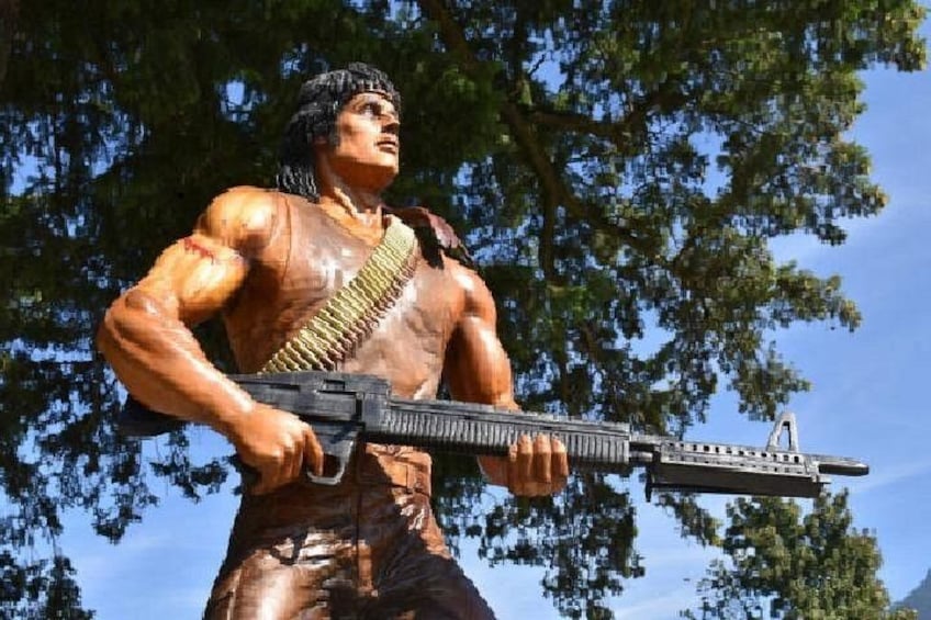 A statue of a muscular figure holding a rifle, with trees in the background. 5