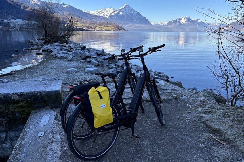 A bicycle with a yellow bag parked by a lakeside with mountains in the background. 3