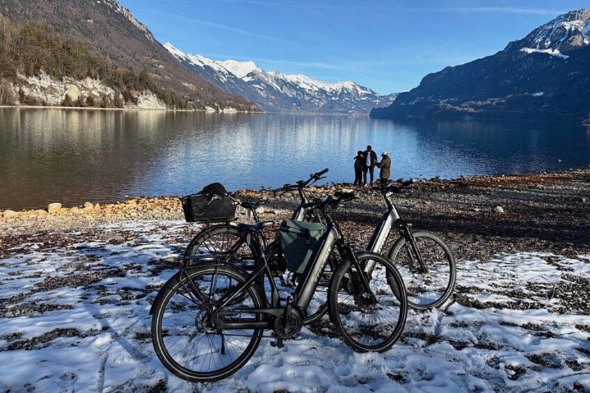 A lake with mountains in the background, a bicycle, and a person standing by the water. 1