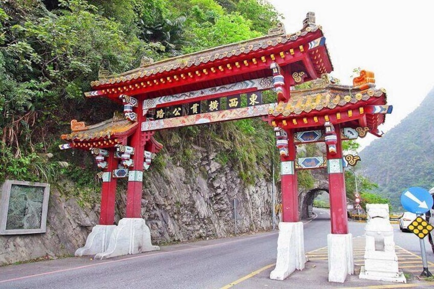 A traditional red and white gate with Chinese characters, set against a mountainous backdrop. 1