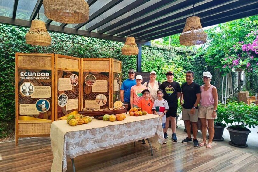 A group of people standing in an outdoor setting with a table displaying fruits and a display board about Ecuador's cocoa origin. 2