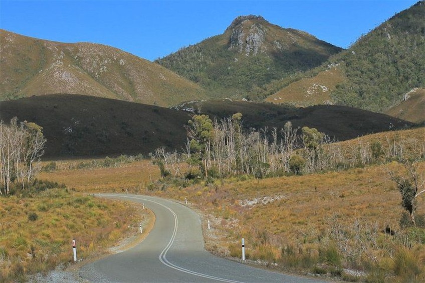 A winding road through a hilly landscape with sparse vegetation and a clear blue sky. 2