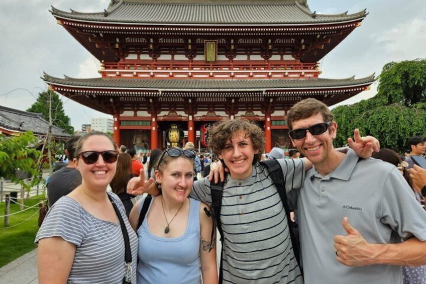 A group of people in front of a traditional Japanese gate with a red roof and multiple tiers. 1