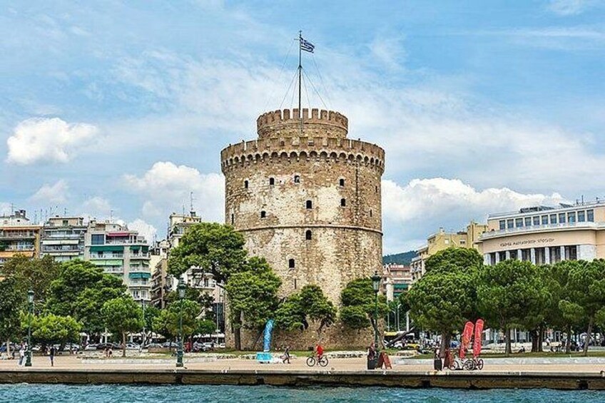 A historic tower with a flag, surrounded by modern buildings and trees. 1