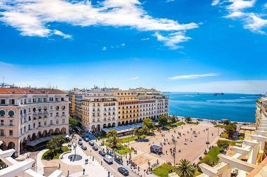 A coastal cityscape with historic buildings, a public square, and the sea. 2