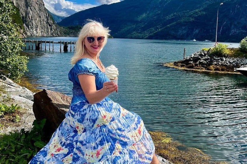 Eine Person in einem blau-weißen Kleid sitzt an einem See, im Hintergrund Berge. 5