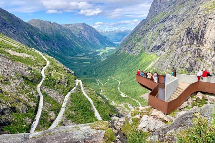 Eine Berglandschaft mit einer kurvenreichen Straße, einer Aussichtsplattform und einem Tal darunter. 4