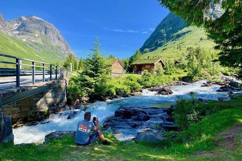 Ein Fluss fließt durch eine gebirgige Landschaft, mit einer Brücke und Ferienhäusern. 3