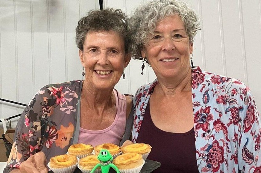 Two people holding a tray with cupcakes and a green toy. 3
