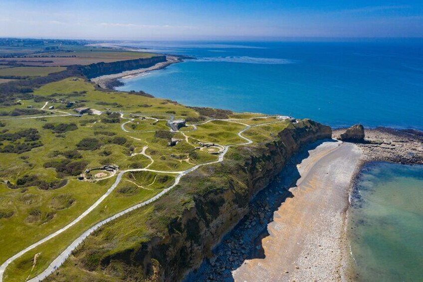 An aerial view of a coastal area with a winding road, grassy fields, a rocky coastline, and a beach. 5